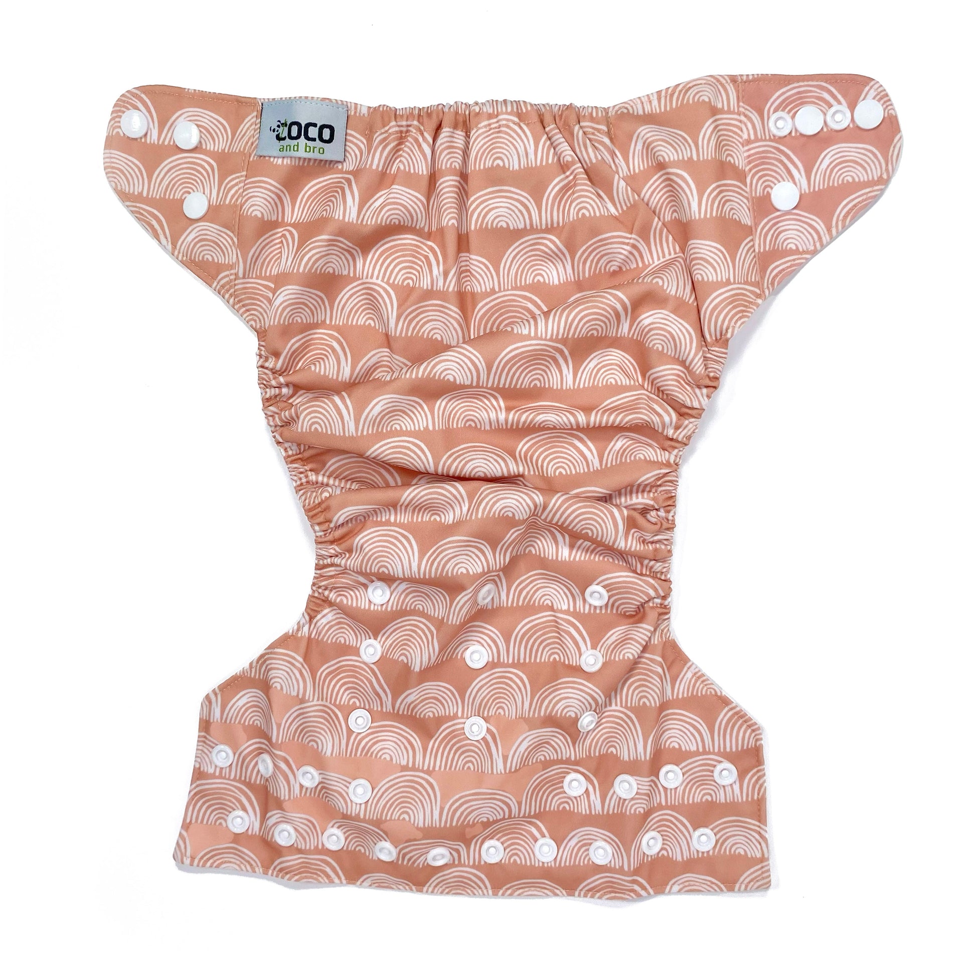 An adjustable reusable nappy for babies and toddlers, featuring a peach rainbow design, with images of white rainbows on a peach background. View shows the full outside pattern of the nappy, with fastenings open.