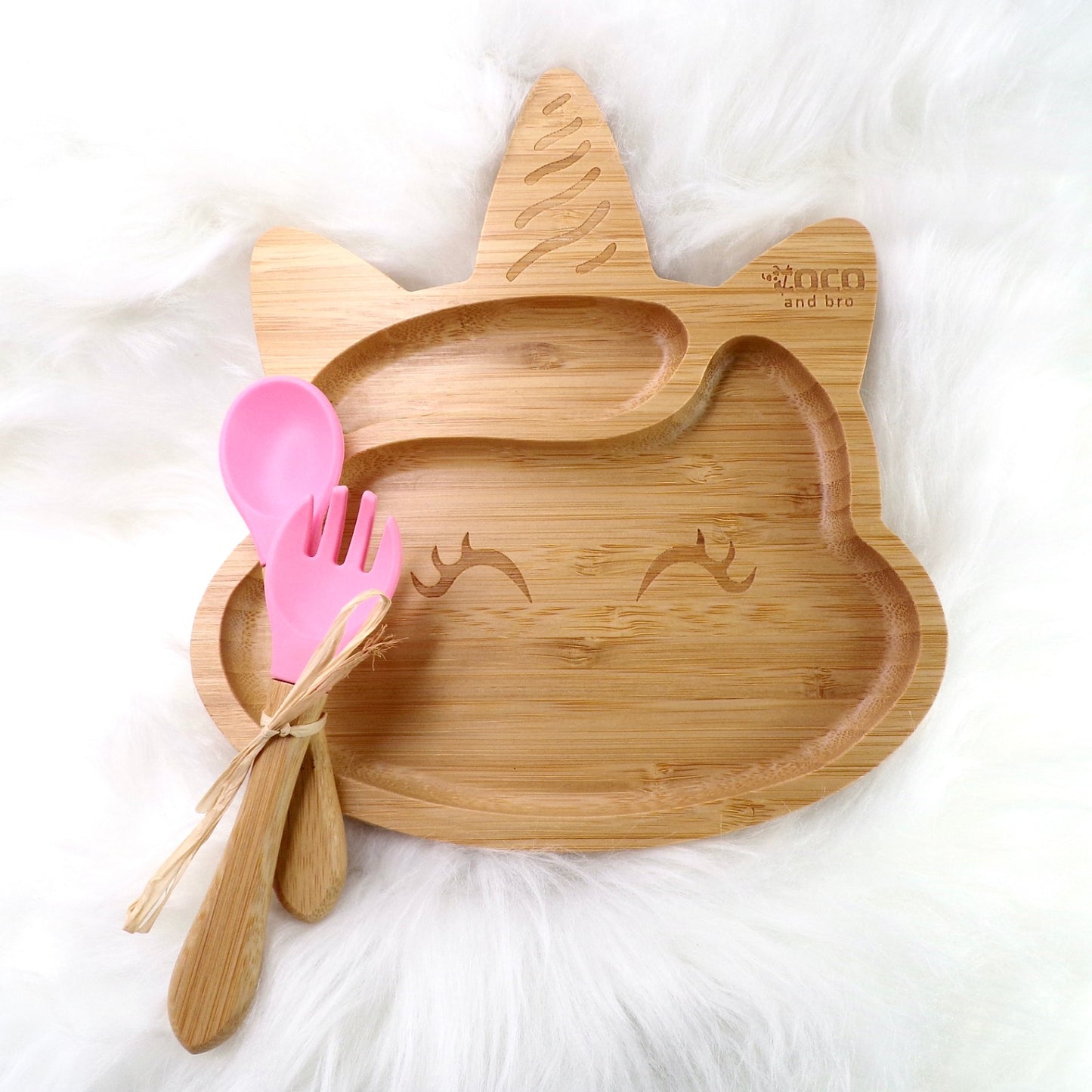 A bamboo children’s plate, with multiple food sections, in a unicorn design. The bamboo plate features a pink silicone suction ring at the back, and includes bamboo fork and spoon utensils in matching colours. Front view.